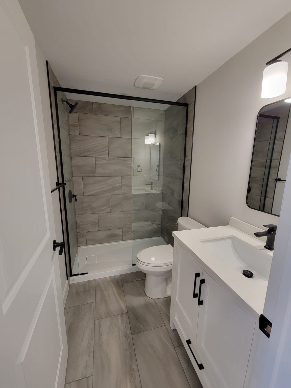 A renovated bathroom with a glass shower, grey tile and matte black fixtures
